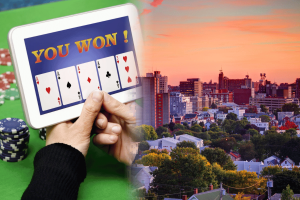 Maine lawmakers push bill banning online sweepstakes casino style games. Hand holding a tablet showing a winning online card game beside poker chips, next to a sunset skyline of Portland, Maine.