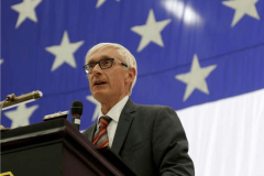 Wisconsin Governor Evers speaking at podium with American flag backdrop addressing tribal mobile sports betting legislation