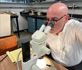 Robert J. Madden examina artefatos sob um microscópio em um laboratório.