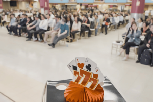 A decorative 777 casino display with playing card aces sits in front of a seated crowd at Resorts World New York City. Resorts World Queens casino to debut first live tables in April