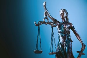 A statue of Lady Justice holding scales in front of a blue background.