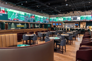 Caesars Sportsbook location with betting counters, seating and large screens showing live sports. Caesars Sportsbook fined $297K for New Jersey violations
