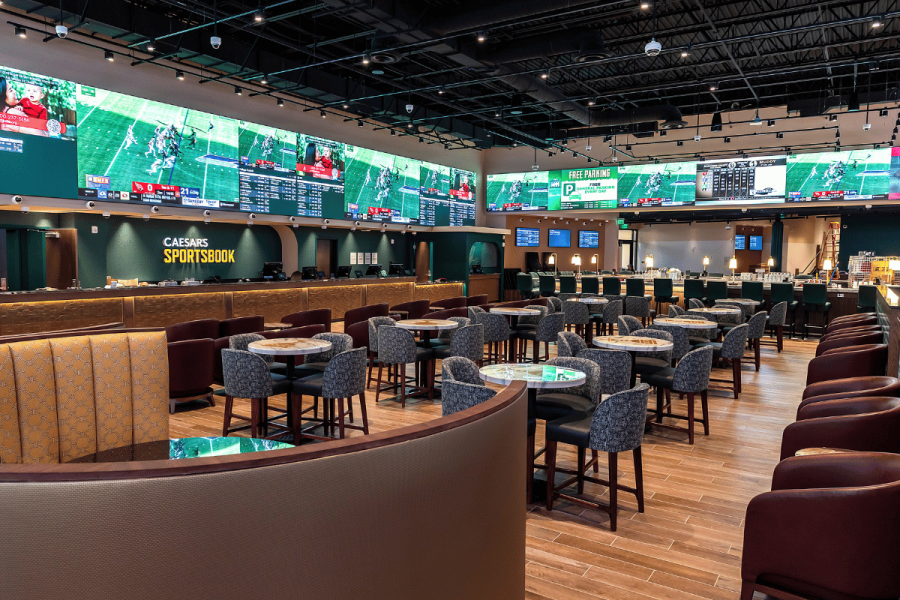 Caesars Sportsbook location with betting counters, seating and large screens showing live sports. Caesars Sportsbook fined $297K for New Jersey violations