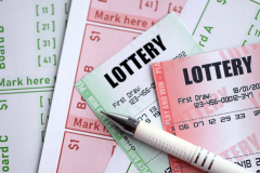 Lottery tickets and betting slips with numbered draw selections and a pen, illustrating lottery gambling and ticket purchases. Massachusetts Lottery faces criticism over youth appeal