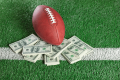 American football on stacks of dollar bills on a field, illustrating NFL betting and prediction market growth.