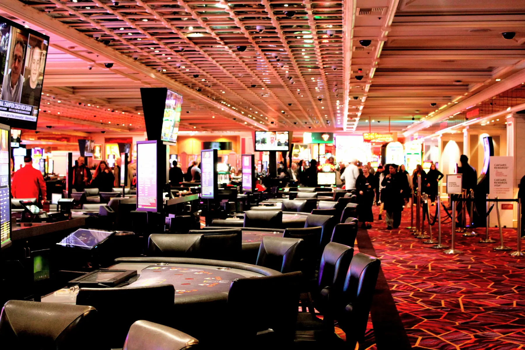A wide view of a casino floor featuring gaming tables, slot machines, and people walking through the venue.